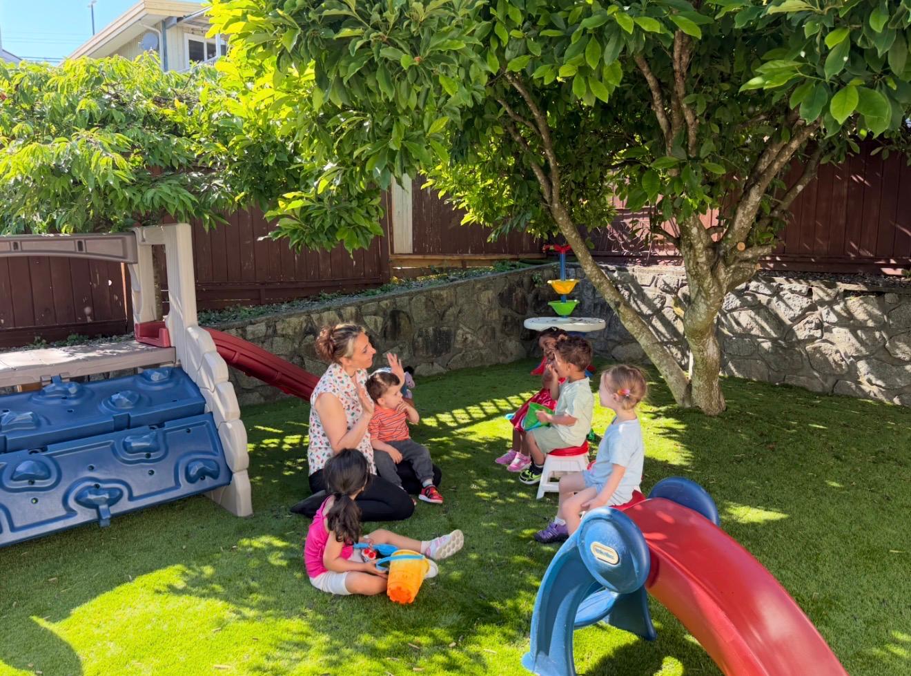 Children and educator sitting together in the outdoor play yard