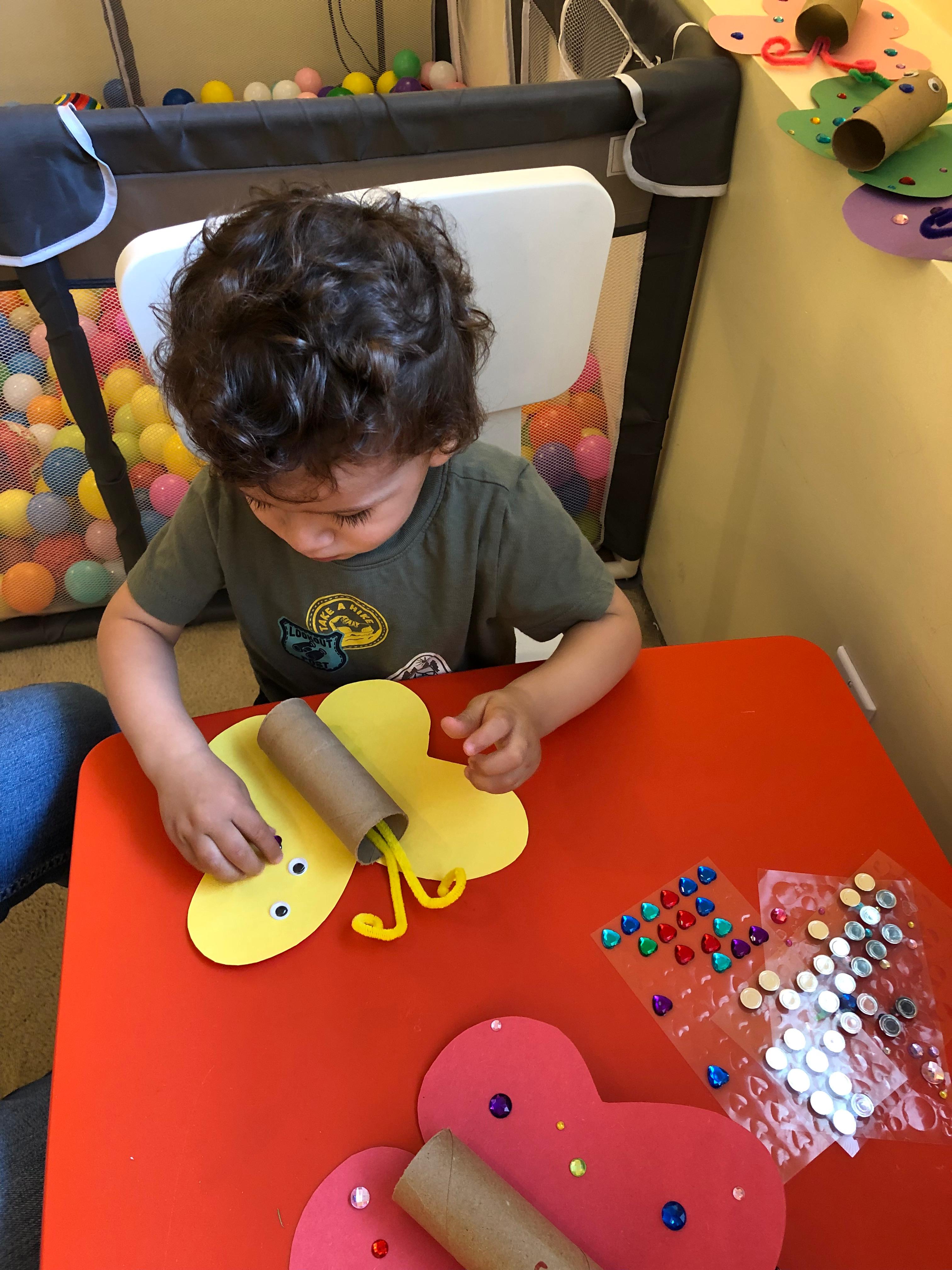 Child making a butterfly craft with paper, gems, and glue
